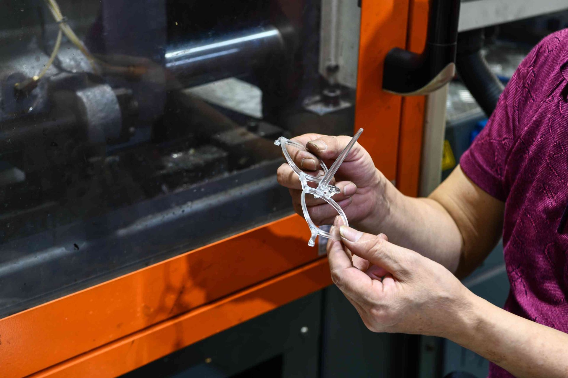 Worker holding a freshly molded transparent TR90 eyewear frame at HAO Eyewear