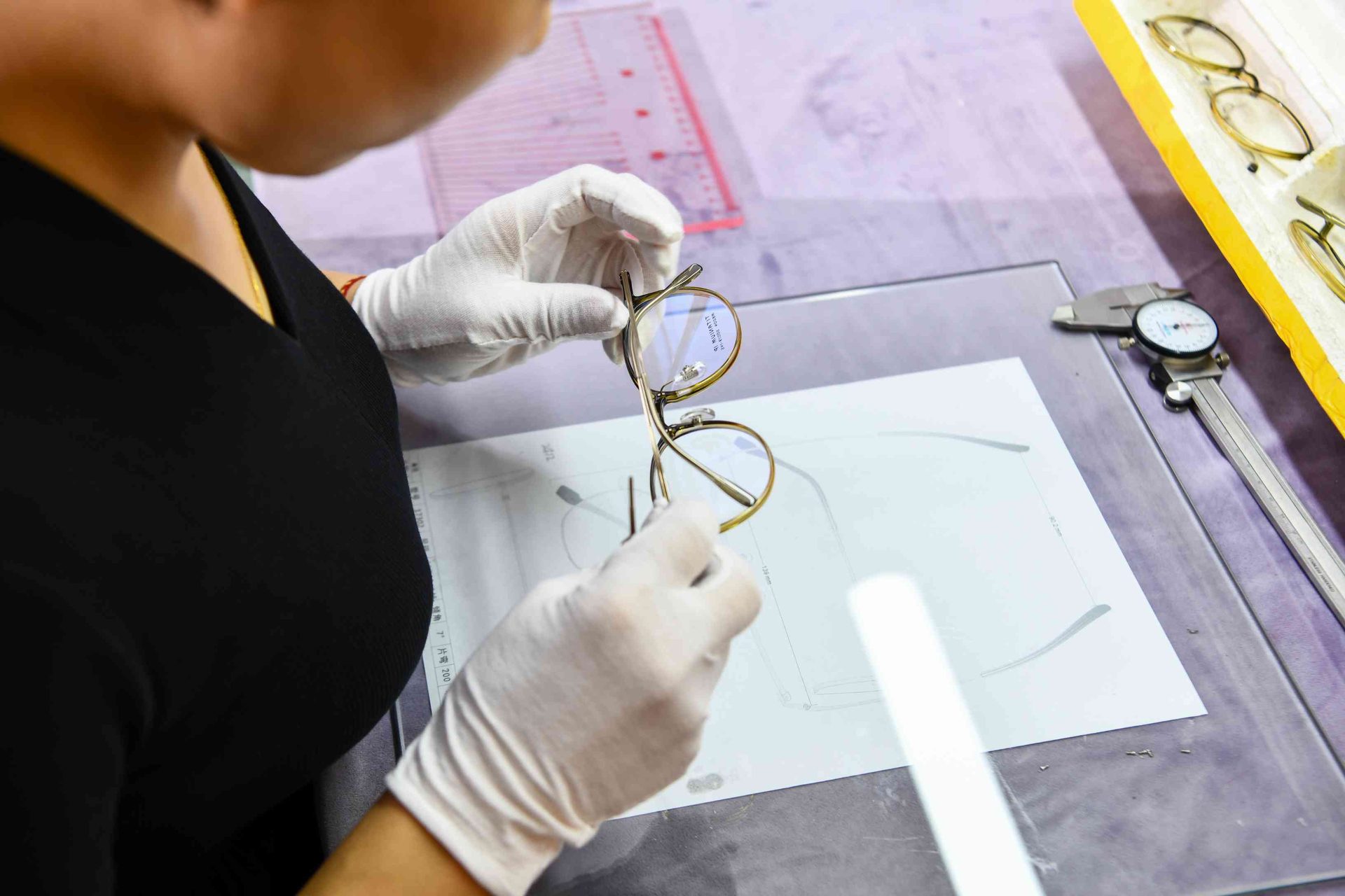 Quality inspector in white gloves examining a finished gold metal optical frame at HAO Eyewear