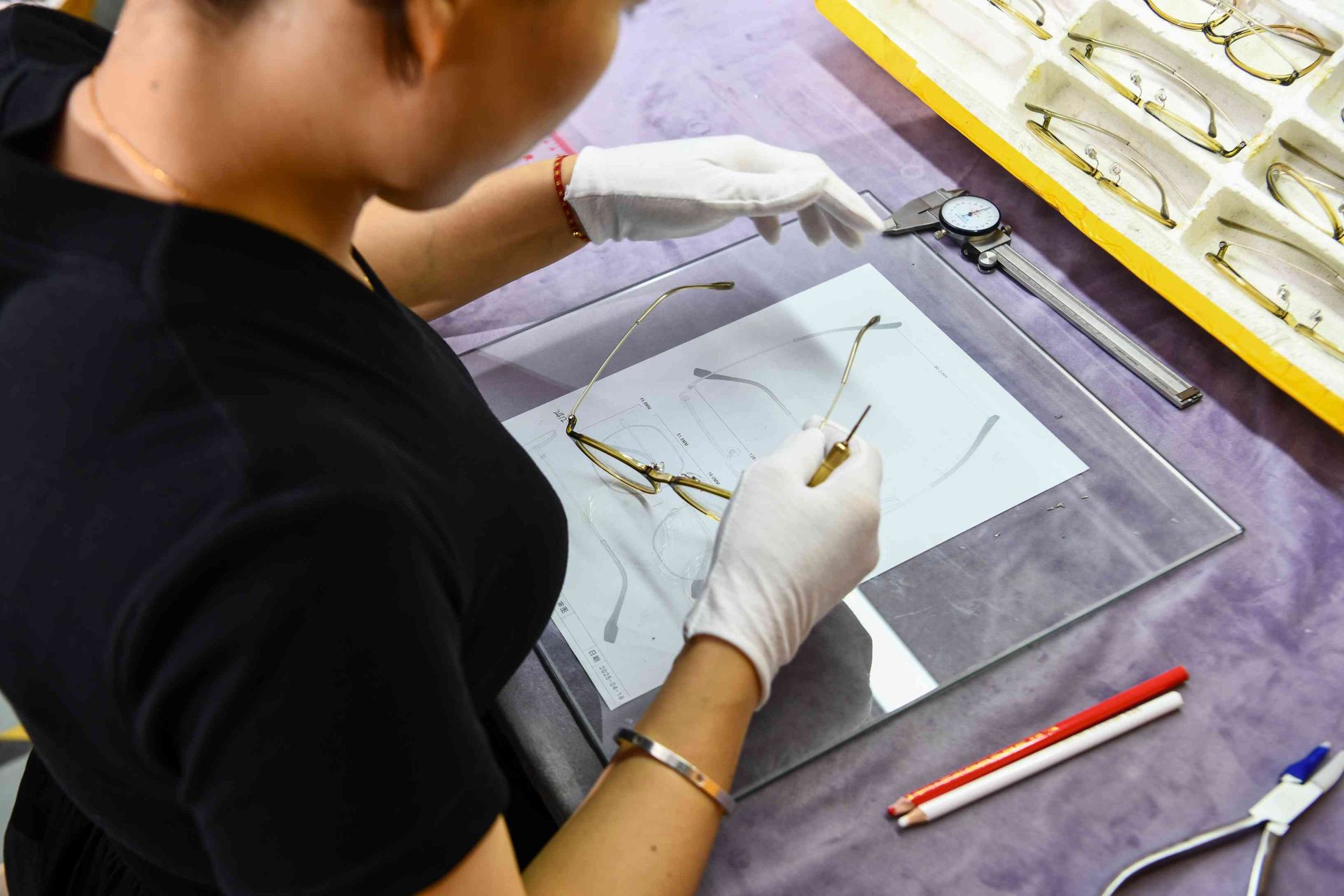 QC inspector checking eyewear frame dimensions against engineering drawings on a light table at HAO Eyewear